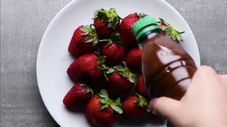 someone squirting chocolate on top of strawberries on a plate