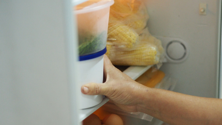 a woman putting a container in fridge