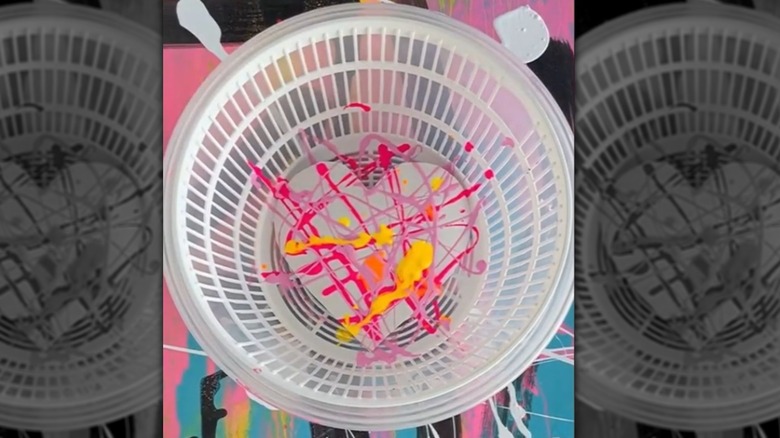 A heart-shaped paper rests on the bottom of a salad spinner with red, pint, and yellow paint splattered on it.