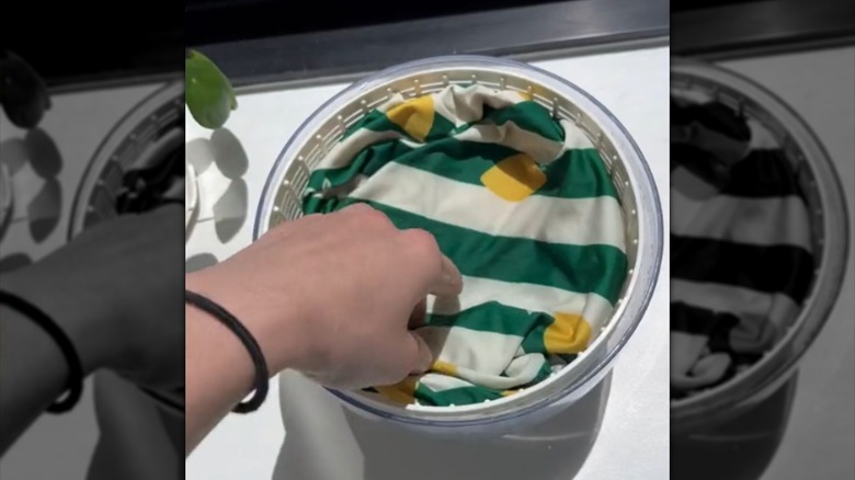 A hand placing a wet swimsuit in a salad spinner to dry.