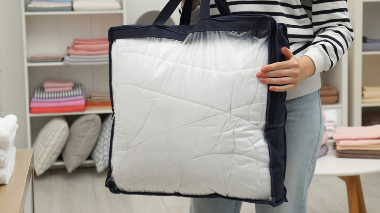 A woman holding a bedding bag with store shelves in the background.