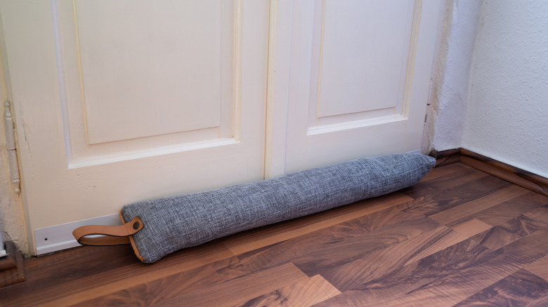 A long gray draft stopper with leather handle detailing