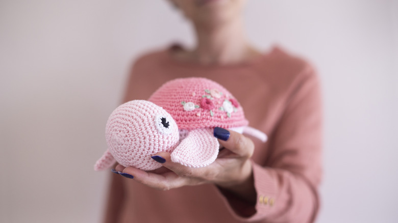 A person is holding a pink crocheted turtle with flowers embroidered on its shell