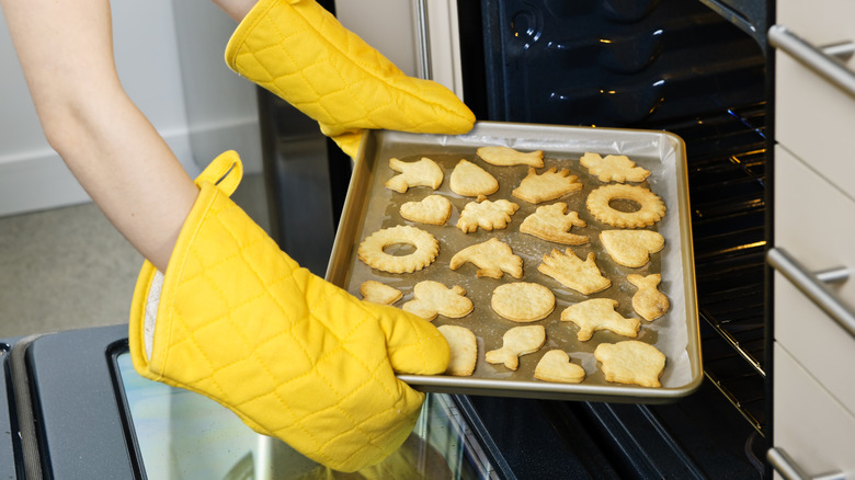 A person taking cookies out the oven wearing quilted yellow oven mitts