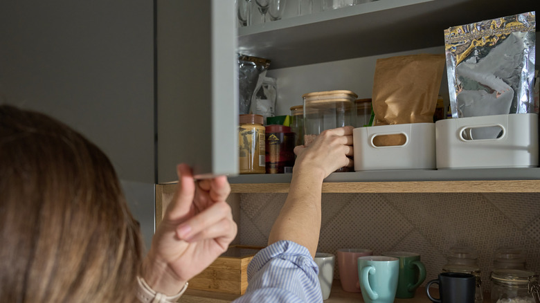 Woman reaching into pantry cabinet shelf for a glass jar.