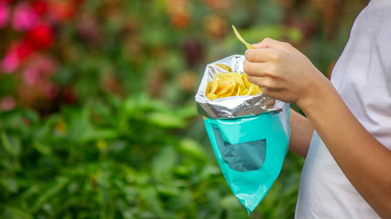 Child's hands holding a potato chip bag outdoors.