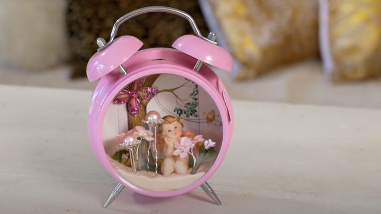An old alarm clock is painted pink with a 3D art scene inside.