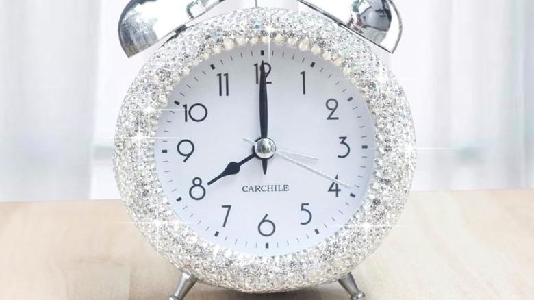 The frame of an old silver alarm clock is covered in rhinestones.