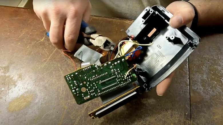 A person uses pliers to pry parts from the inside of a digital alarm clock.