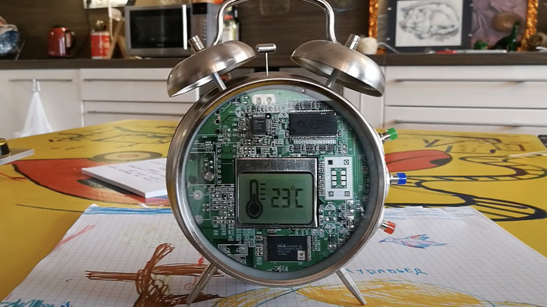 An old alarm clock made into a weather station sits on a tabletop in a kitchen.
