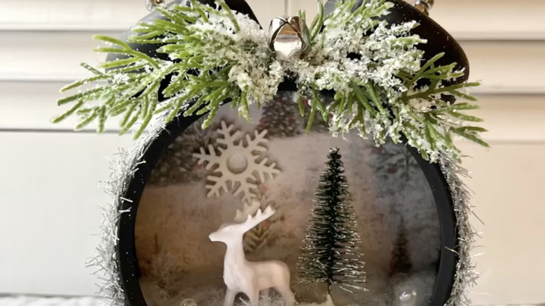 A face of an old alarm clock is removed and replaced with a winter scene, while the outside is adorned with snowy pine needles.