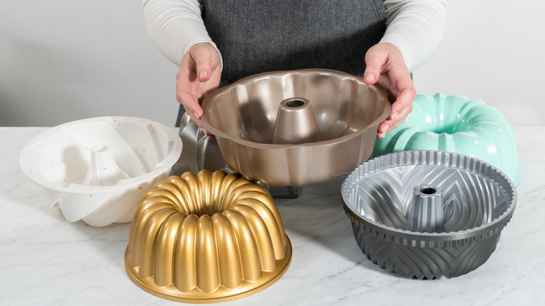 A woman displaying different sizes, designs, and colors of bundt pans