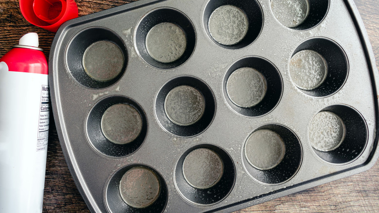 close up of metal muffin tin next to oil spray on counter