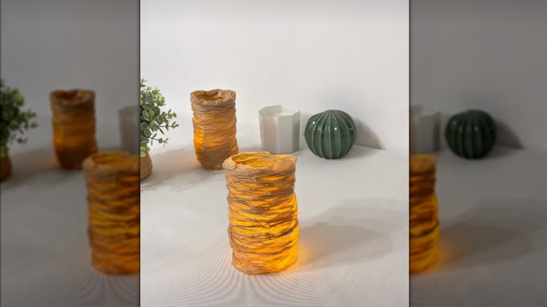 Two candle-lit lanterns created with scrunched parchment paper sit on a white tabletop alongside other decorations.
