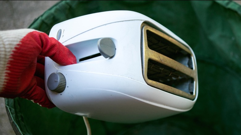 Gloved hand pulling old white toaster from trash can
