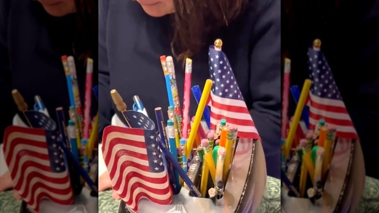 Woman sitting behind toaster with pencils and small flags in slots
