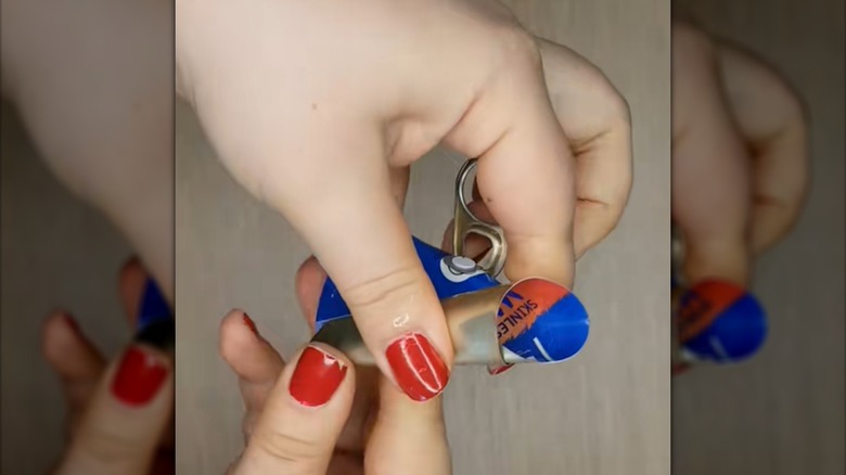 A person rolls the metal lid from a tin can into a cone shape.