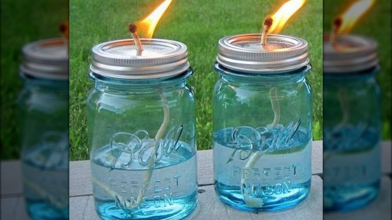 Two blue mason jars with lit wicks.