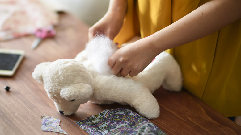 person restuffing a white teddy bear