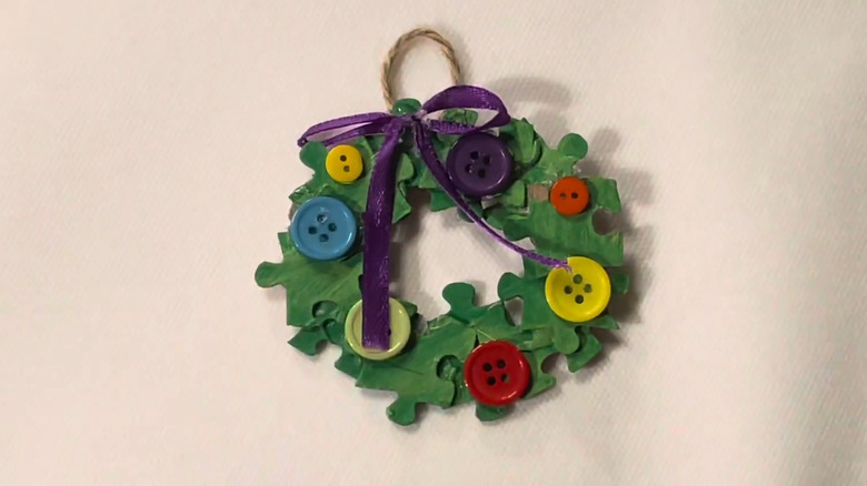 Green wreath ornament with twine created with puzzle pieces and small buttons of various colors