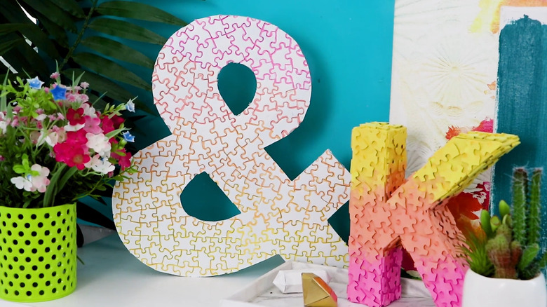 Colorful ampersand and K letter covered with puzzles on a shelf next to plants