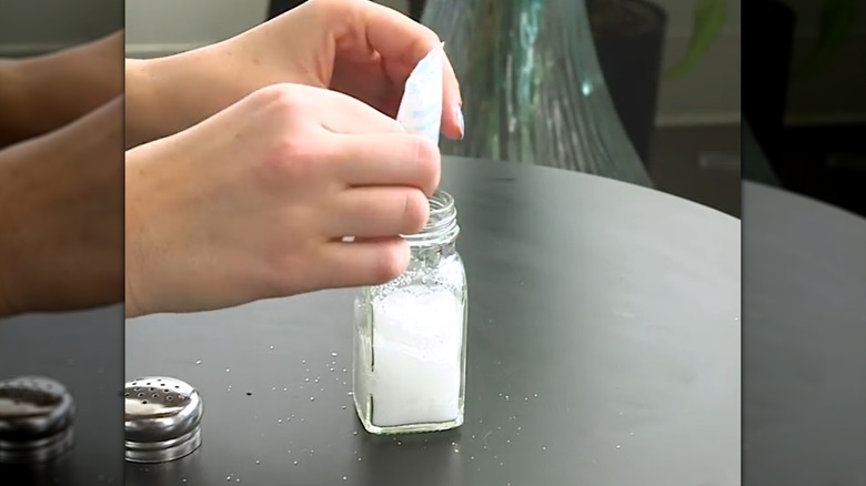 Person putting a silica gel packet in a salt shaker