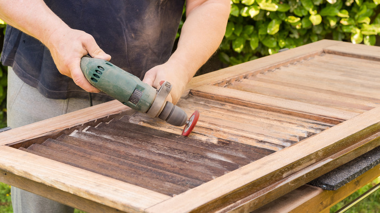 A person sands a wooden shutter outside.