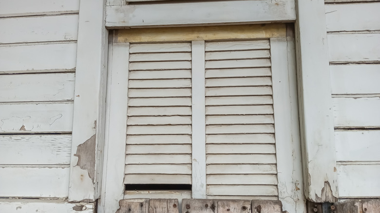 Broken louvered window shutters on a weathered building.