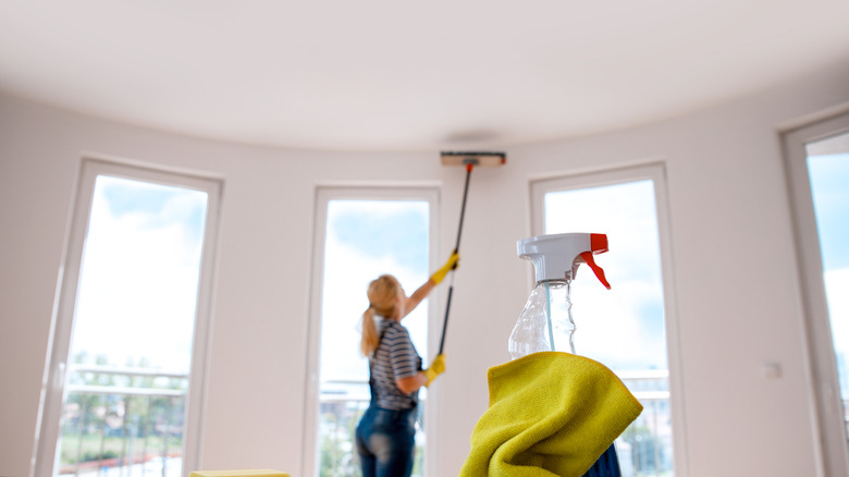 Woman cleaning her ceiling with a push broom.