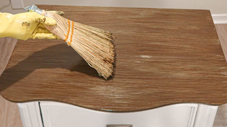 Someone using a broom head to stain a side table.
