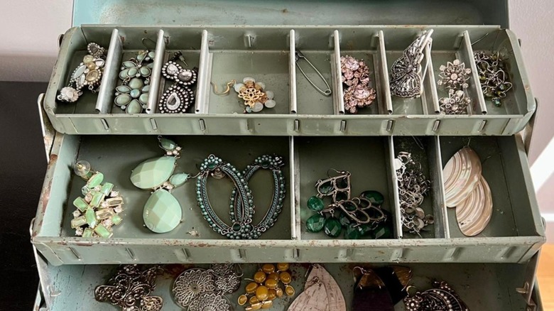 A green metal tackle box filled with jewelry and accessories.