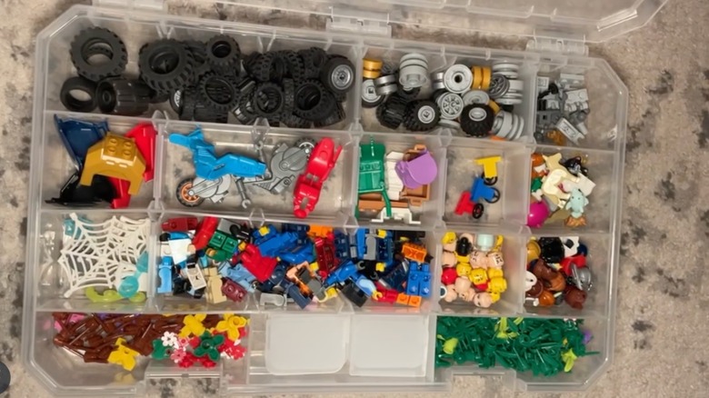 A clear box holding different building blocks and toy parts.