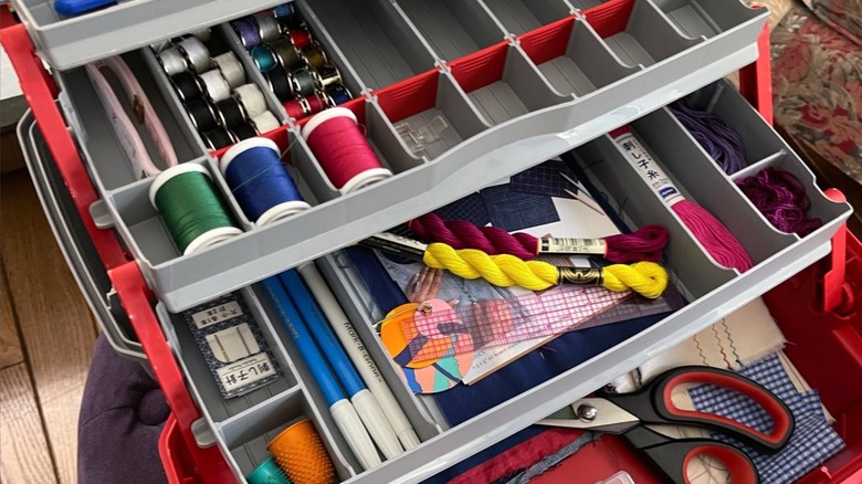 A open tackle box with different thread spools and sewing supplies inside.
