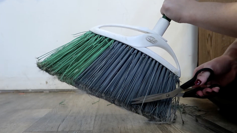 A close-up of hand trimming ends of broom bristles