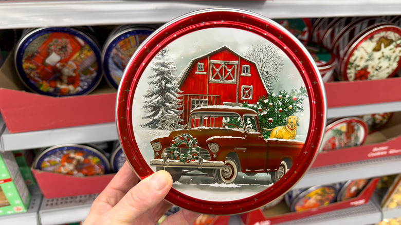 A hand holds a new Christmas-themed cookie tin in front of some store shelves.