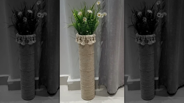 A boho-style planter in room with faux plant inside the top and curtains in the background.