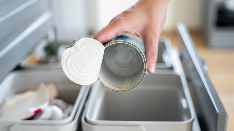 A person tossing an empty tin can into the trash.