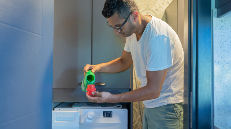 A man wearing glasses pours detergent to do a load of laundry.