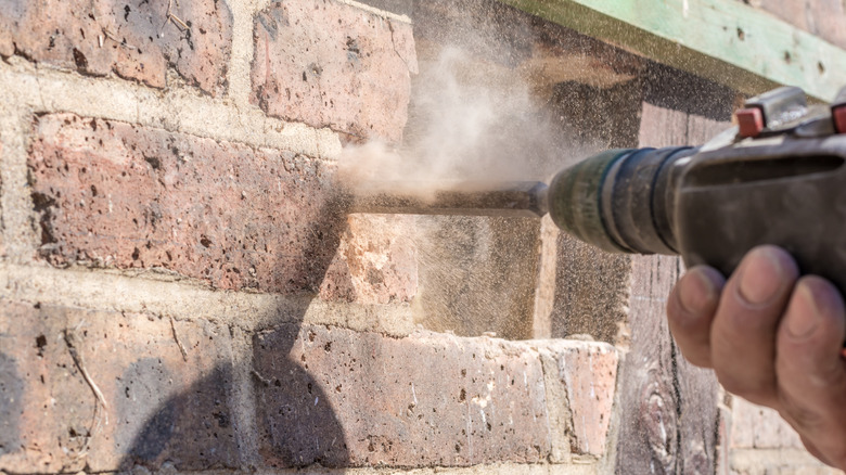 Hand holding onto power tool and drilling hole in brick