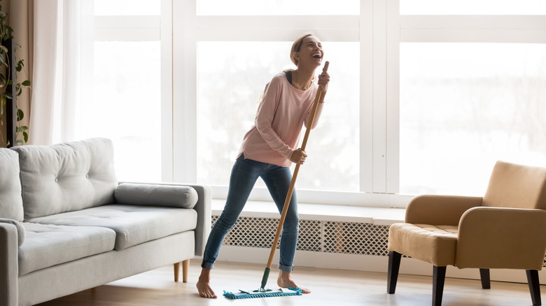 Person holding mop in living room while singing and pretending it is a microphone
