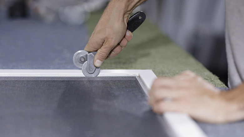 A person repairing a window screen with proper tools