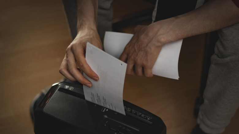 Man putting documents into a black paper shredder.