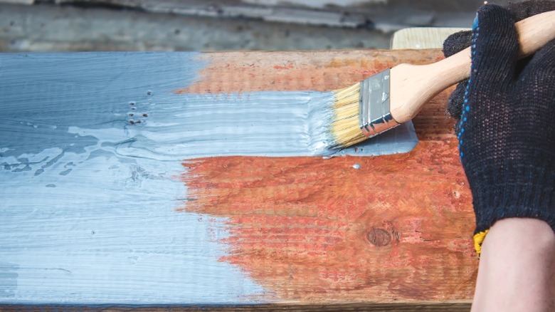 person painting over wood board with blue-gray paint