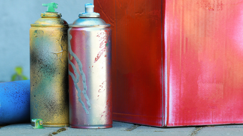 Old spray paint cans sit next to a red-painted cardboard box.