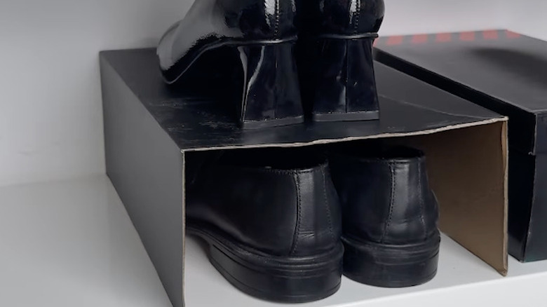 Two pairs of shoes sit in and on top of a cut-up shoebox in a closet.