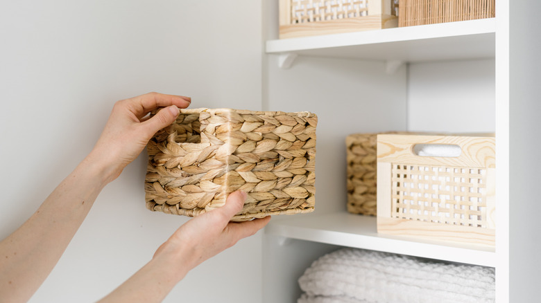 A person puts a woven basket back onto a built in bookshelf beside other storage bins.