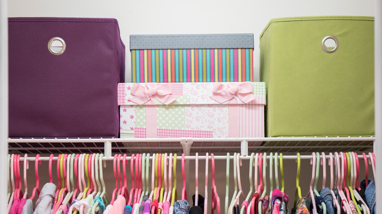 Row of stuffed animals stored inside grey fabric bins with rope cords underneath toddler bed or crib. Animals include pink bunny, pink bear, and a leopard.