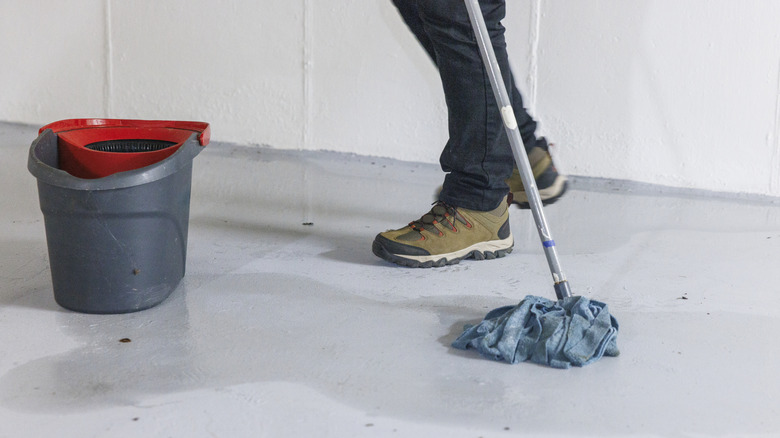 Person mopping up white basement floor after flood