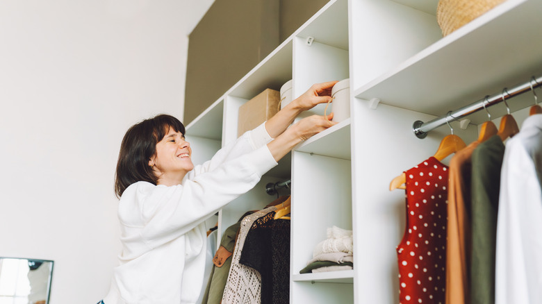 A woman places a box on a closet shelf