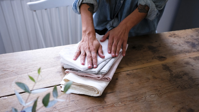 A person's two hands on top of pile of cloth napkins on a table